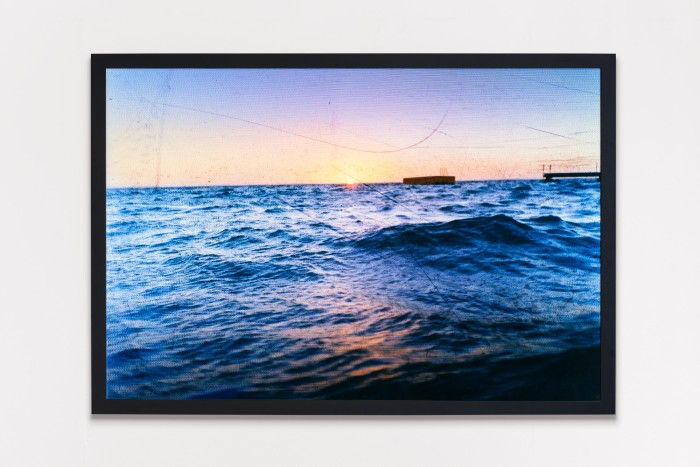 A framed photo of the sea at sunset with a jetty and pontoon in the water