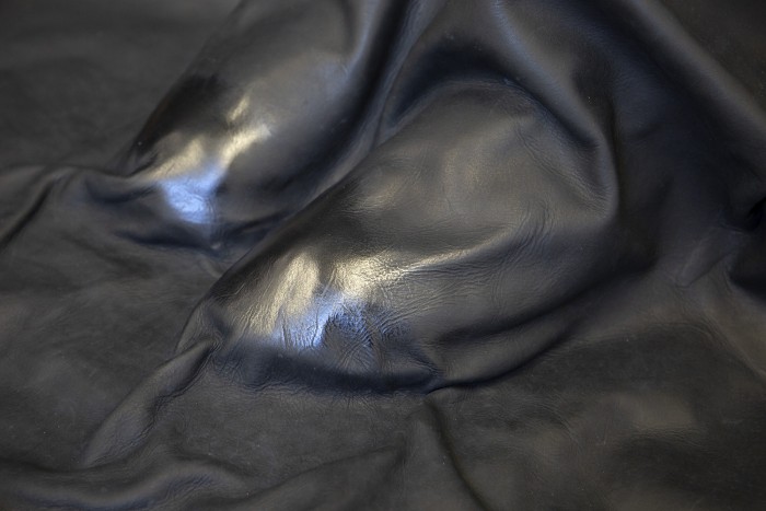 A close up photograph of boots under a shroud of black leather. The toes are polished to a shine, contrasting with the matte finish of the rest of the leather.