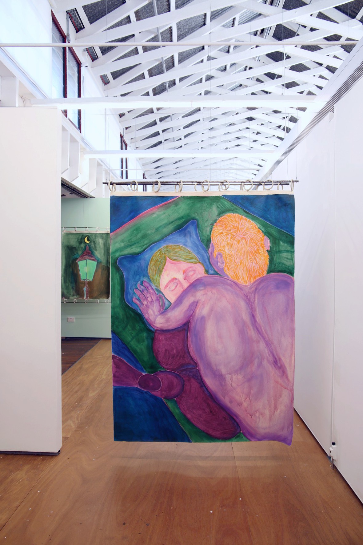 a painting of two purple figures engage in love making on green sheets from a birds eye view perspective hangs from ceramic rings and a pole like a curtain. It is installed in a bright room