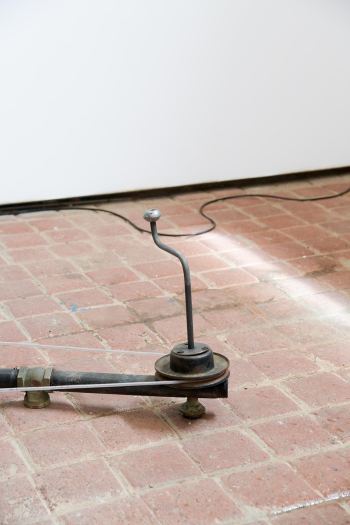 a small pulley with a crank handle sits on a pink brick floor, illuminated by sharp sunlight.