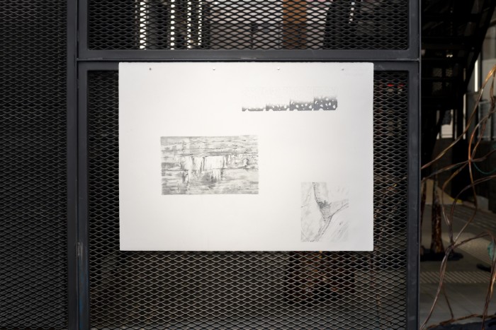 a large piece of white paper hangs on a black architectural metal grate. The paper has delicate graphite drawings on three sections of the page.