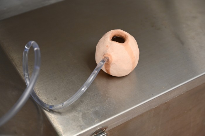 a small bisque-fired clay vessel leaks water that is fed into it thorugh clear pvc tubing.