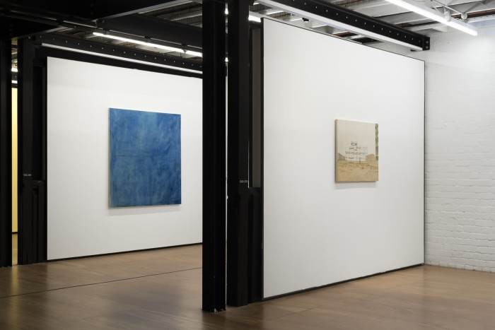 Installation view of big blue mostly square painting and smaller landscape scaffolding painting on parallel walls of different booths.