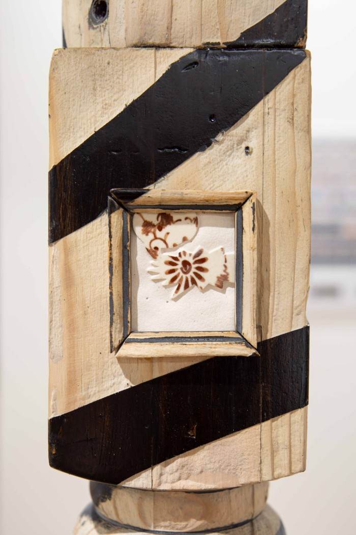 A tiny ceramic tile is inlaid in an equally tiny frame in the side of a vertical table leg. The outlines of word bubbles are in the tiles, showing the original pattern that was sandblasted off.