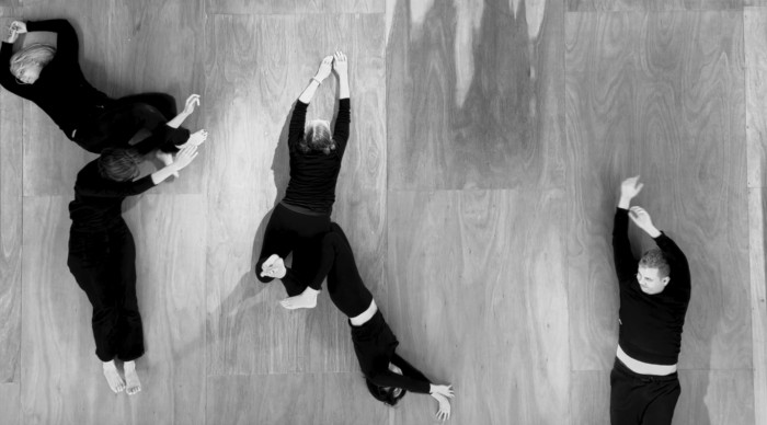 A black and white photo of five people wearing all black clothes rolling along a wooden floor.