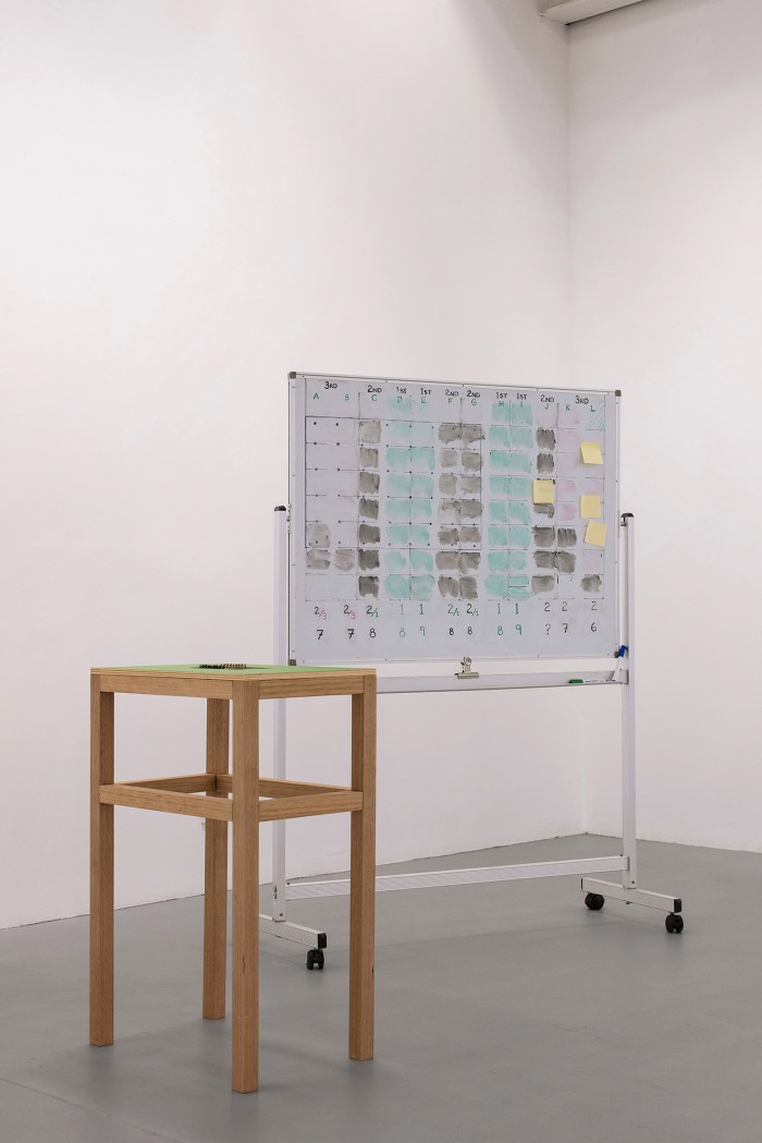 A small waist height table with a bright green surface is inlaid with a computerised chess-set. Behind this stands a whiteboard with a diagrammatic drawing on it.